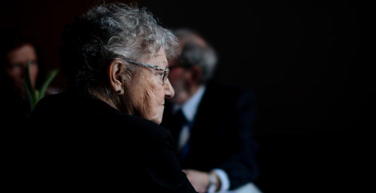 An older lady sitting sitting on stage with other older people