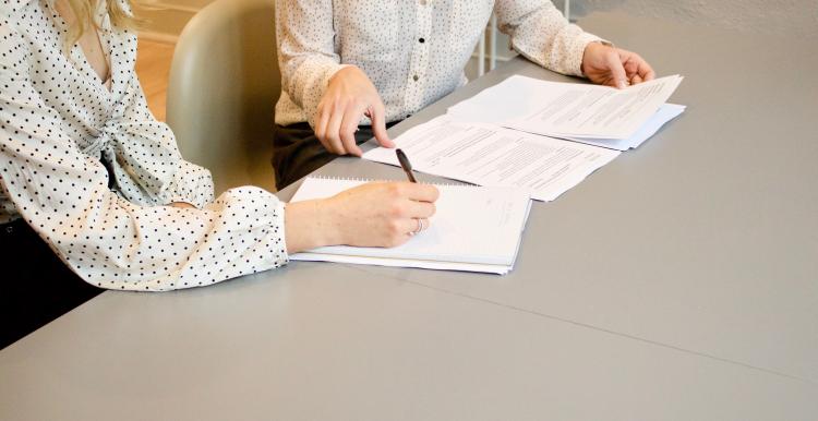 Two people talking over a document. They are sitting at a large table.